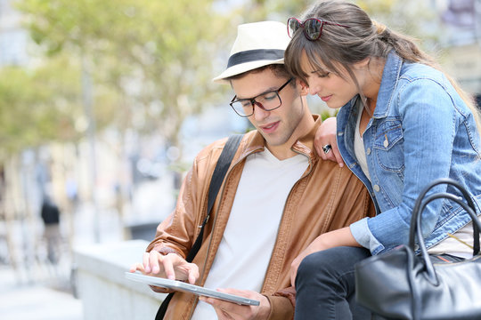 Trendy young couple connected on tablet and smartphone in town