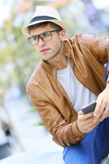 Hipster guy using smartphone sitting on public bench