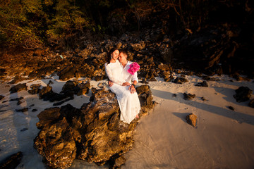 bride and groom at beach against rocks at sunrise