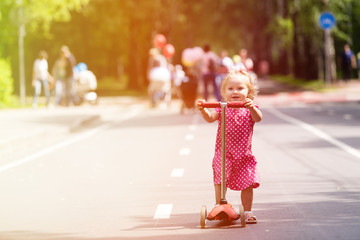 happy little girl learning to ride scooter in the city