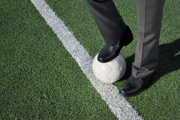 Homme en costume, debout sur un terrain de football, un pied sur un ballon de football