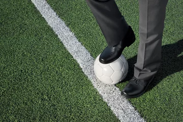 Crédence de cuisine en verre imprimé Foot Homme en costume, debout sur un terrain de football, un pied sur un ballon de football