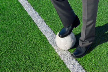 Man in suit, standing on a soccer field, one foot on a soccer ball