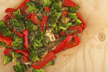 Vegetables mix baked in the oven on paper on the wooden table with aubergine, red bell pepper, brussels sprout, pumpkin seeds, basil and olive oil.