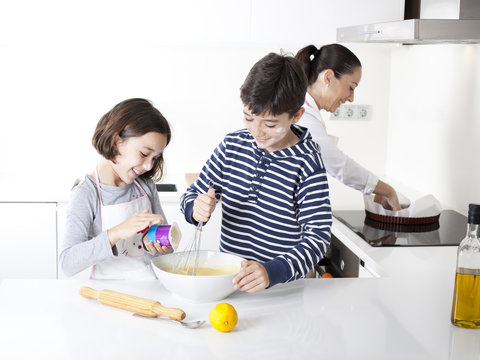 Niños cocinando torta mientras su madre prepara el recipiente