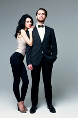 Handsome man in suit and pretty brunette female model on grey background
