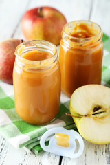 Jars of baby puree with apples on white wooden background
