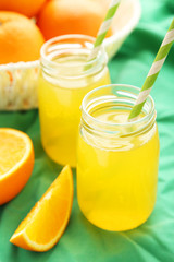 Orange juice in bottle and orange in basket on green background