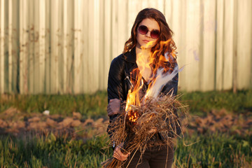 Serious girl in sunglasses standing in a black jacket with a fire in his hands Outdoors