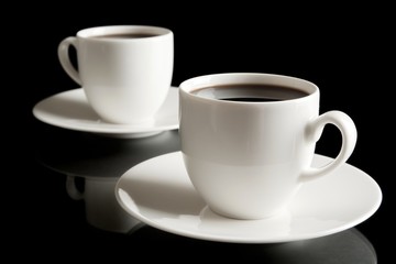 Cups of coffee with saucer isolated on black