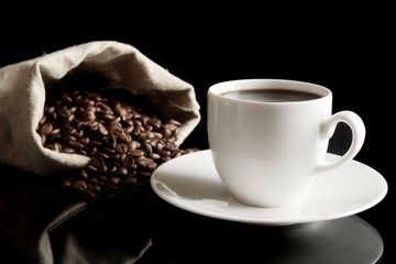 Cup of coffee with saucer with bag with coffee beans on black