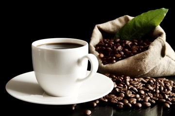 Cup of coffee with bag and coffee beans with green leaf on black