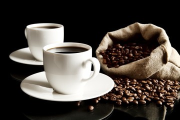 Cups of coffee with saucer with bag with coffee beans on black