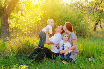 Fototapeta premium Father, mother and two sons are playing in the garden on sunset
