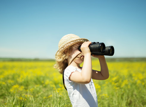 Little blonde girl in straw hat looking through binoculars outdo
