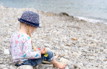 Blond Girl Sitting on Rocky Beach Looking at Water