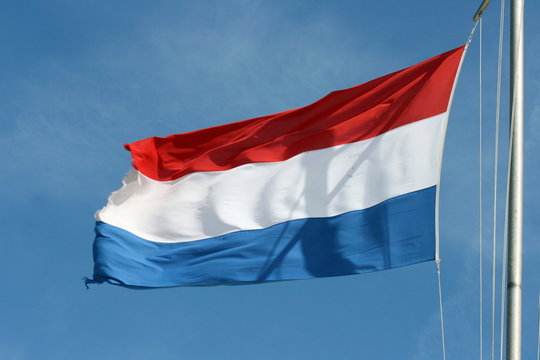 Flag of the Netherlands with blue sky in the background
