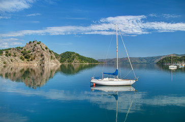 Fototapeta na wymiar white yacht in sea near rocky island with mountains and small ma