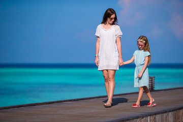 Little girl and young mother walking on wooden jetty at exotic