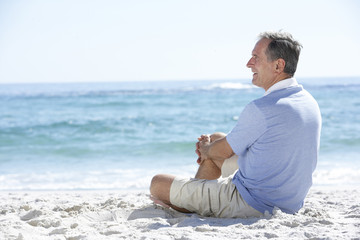 Senior Man On Holiday Sitting On Sandy Beach