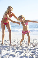 Mother And Daughter Running Along Beach Together Wearing Swimming Costume