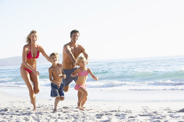 Fototapeta na wymiar Young Family Running Along Beach on Holiday
