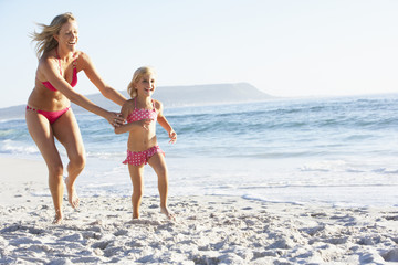 Mother And Daughter Running Along Beach Together Wearing Swimming Costume