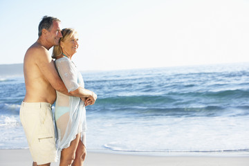 Senior Couple On Holiday Running Along Sandy Beach Looking Out To Sea