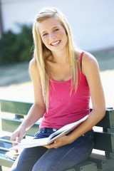Female College Student Sitting On Bench Reading Textbook
