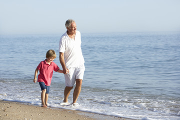 Grandfather And Grandson Enjoying Walk Along Beach