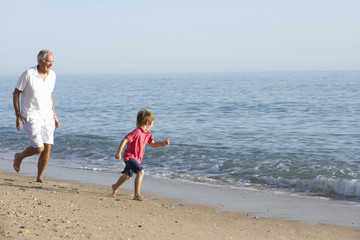 Grandfather And Grandson Running Along Beach