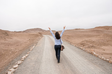 Young woman walking in the road with raised arms 