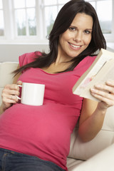 Pregnant Woman Drinking Hot Drink And Reading Book At Home