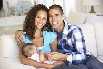 Young Family With Baby Relaxing On Sofa At Home