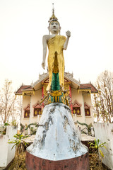 Obraz premium Standing buddha statue front of church of Wat Phra That Doi Gongmoo in Maehongson, Thailand, under white cloudy sky