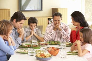 Extended Hispanic Family Saying Prayers Before Meal At Home - Powered by Adobe