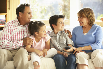 Hispanic Grandparents With Grandchildren Relaxing On Sofa At Home