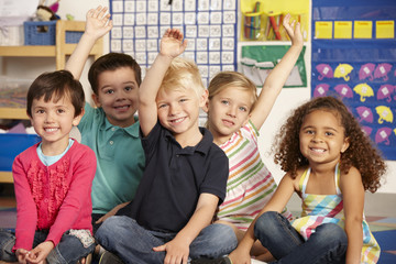 Group Of Elementary Age Schoolchildren Answering Question In Class