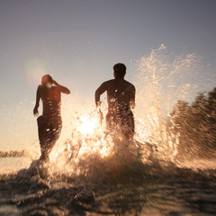 Glückliche junge Menschen laufen und springen am See beim Sonnenuntergang