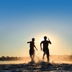 Glückliche junge Menschen laufen und springen am See beim Sonnenuntergang © Thaut Images