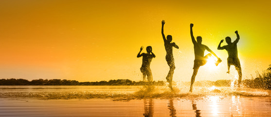 Glückliche junge Menschen laufen und springen am See beim Sonnenuntergang