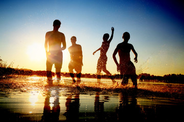 Glückliche junge Menschen laufen und springen am See beim Sonnenuntergang