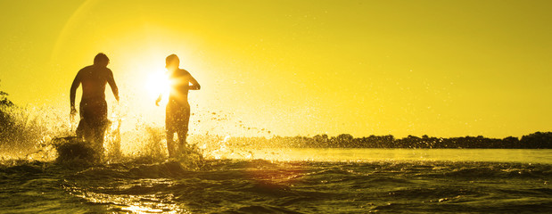 Glückliche junge Menschen laufen und springen am See beim Sonnenuntergang