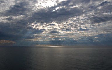 Sunshine make a way through clouds over a sea surface.