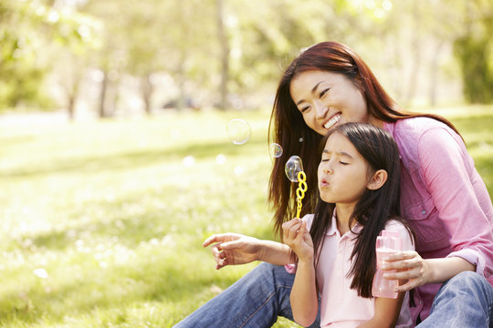 Asian mother and daughter blowing bubbles in park