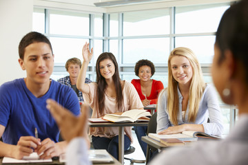 Multi racial teenage pupils in class one with hand up
