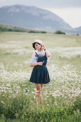 Beautiful young woman in a straw hat posing in a camomile field