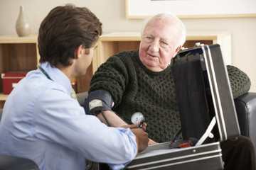 Fototapeta na wymiar Doctor taking senior man's blood pressure at home