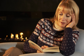 Mature woman reading in front of fire at home