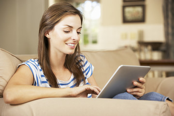 Woman Sitting On Sofa At Home Using Tablet Computer